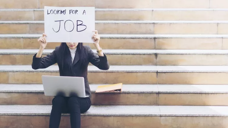 Une jeune femme tient une pancarte "looking for a job"